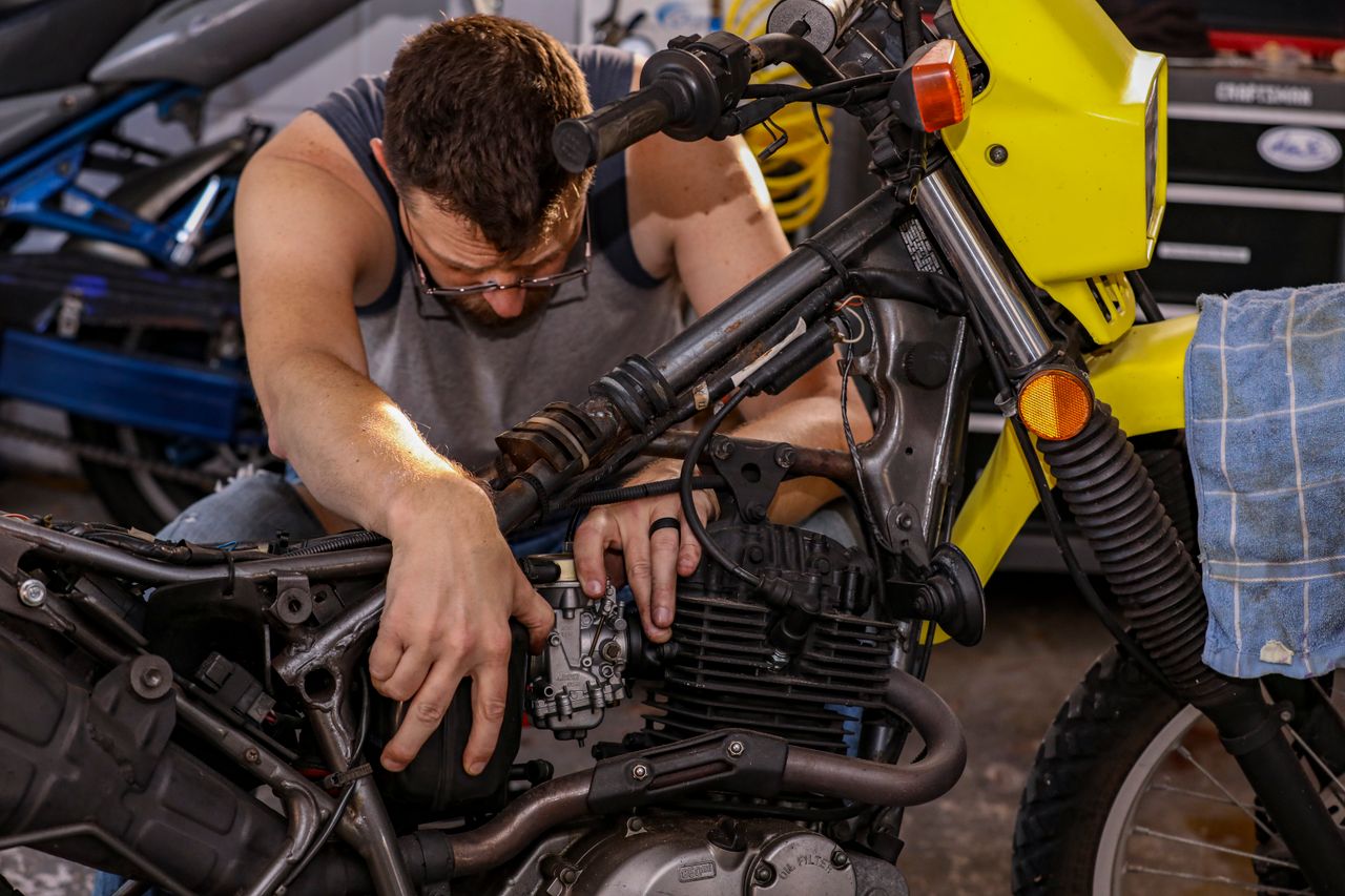 Mechanic intricately repairing motorcycle engine in a garage environment.