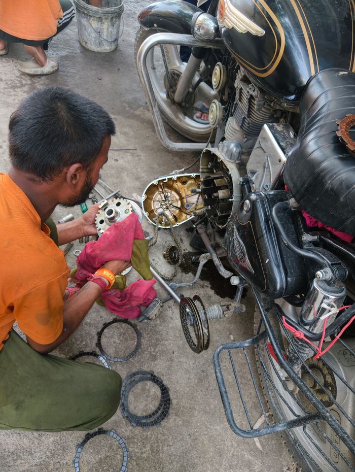 Mechanic working on motorcycle engine parts outdoors. Close-up of hands with tools and engine components.