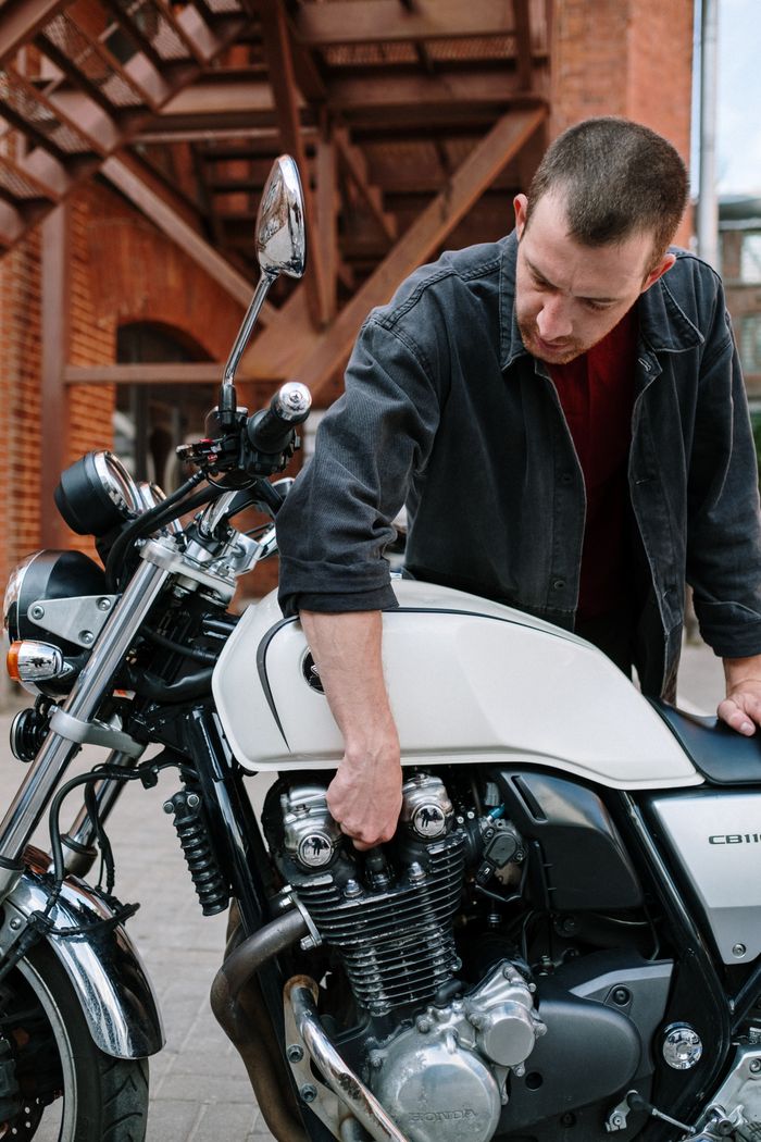 Mechanic inspecting motorcycle engine outside a rustic building.