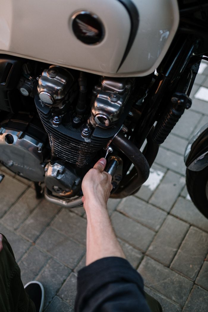 Close-up of a mechanic's hand fixing a motorcycle engine outdoors.